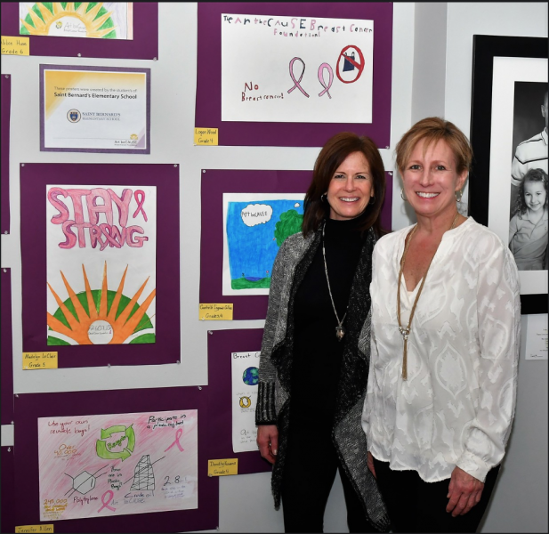 2 women smiling in front of pink ribbon art