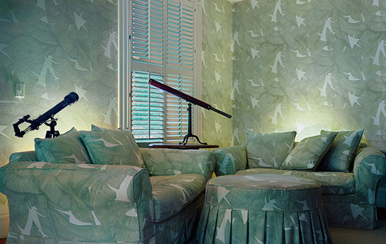 Untitled Interior (Telescopes), From Second Nature Series, 2011 A living room with Green leaf pattern material on the walls, furniture there are 2 telescopes by the single window in the room