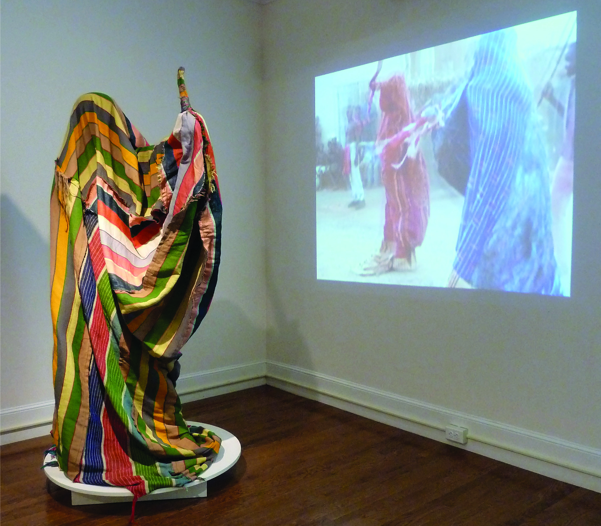 James Friday, “Dead Father” Masquerade Costume Costume made from colorful striped cloth is display next to a video showing the costume in motion