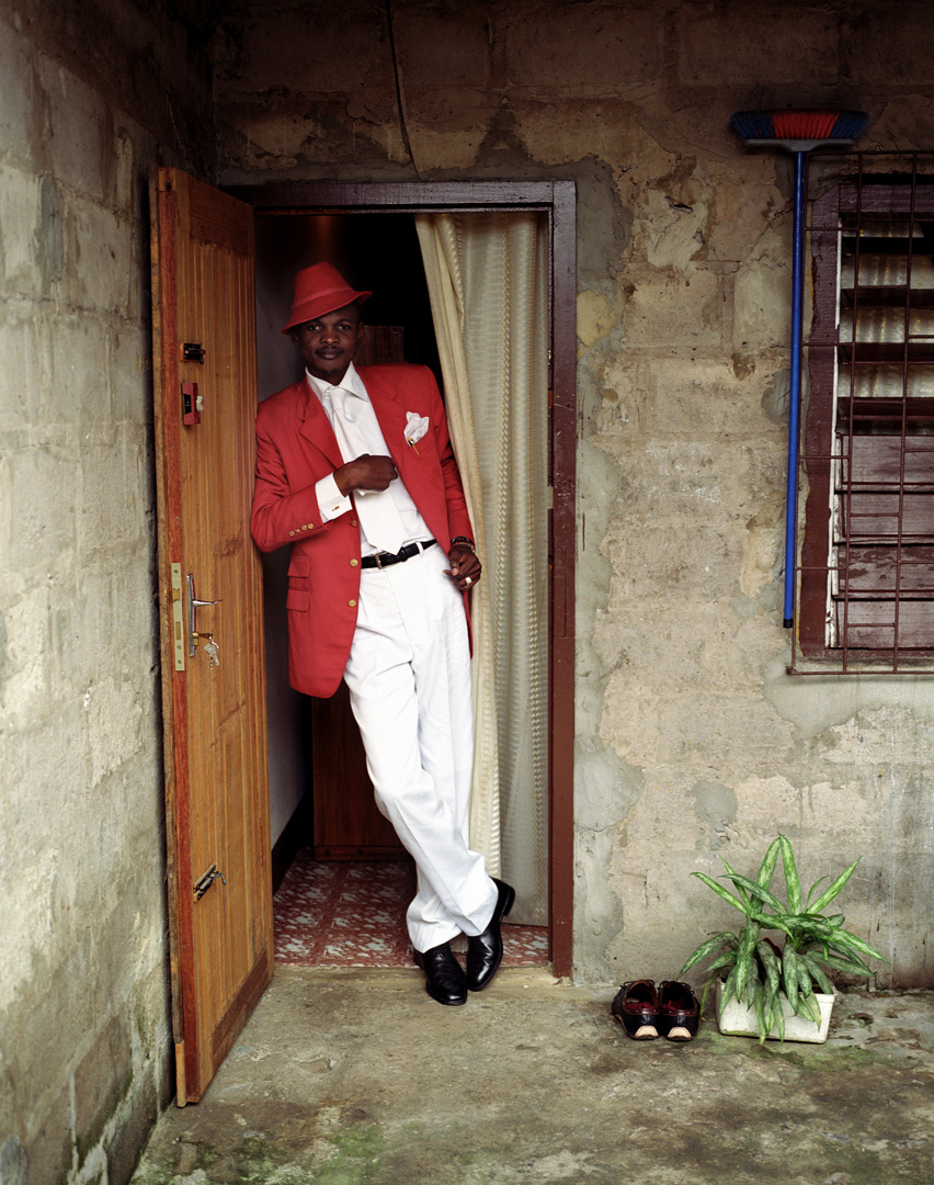 Hector Mediavilla, “Delagrace, aka The Icon of Beautiful Color” Photograph: The sapeur Delagrace, also known as the icon of beautiful colors, poses in the entrance to his room.